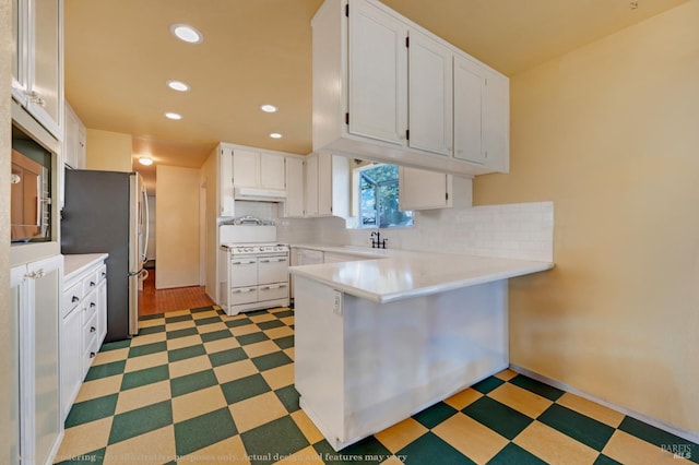 kitchen with freestanding refrigerator, a peninsula, under cabinet range hood, double oven range, and light floors