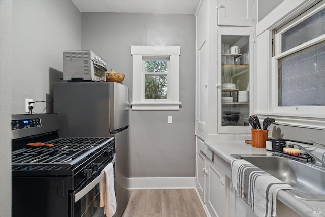 kitchen with sink, stainless steel gas range, white cabinets, and light wood-type flooring