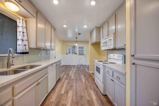 kitchen with sink, white appliances, hanging light fixtures, tasteful backsplash, and light wood-type flooring