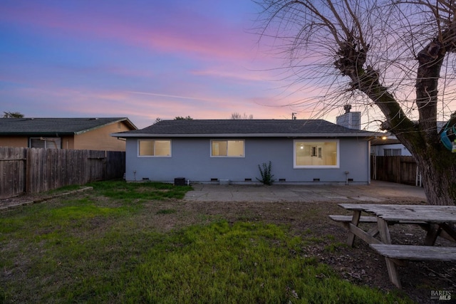 back house at dusk featuring a patio area and a lawn