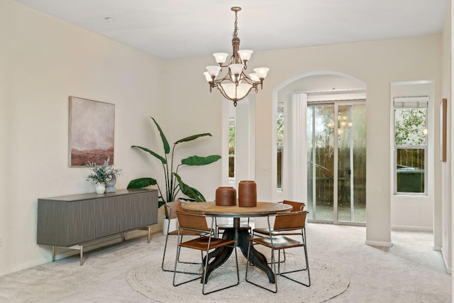 carpeted dining area featuring baseboards, arched walkways, and a notable chandelier