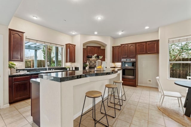 kitchen with double oven, light tile patterned flooring, a kitchen island, and a wealth of natural light