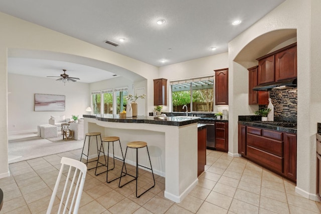 kitchen with ceiling fan, light tile patterned floors, under cabinet range hood, visible vents, and a kitchen breakfast bar