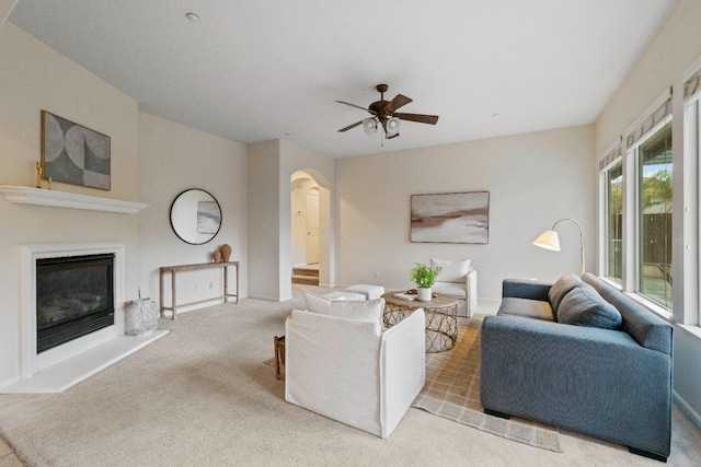 carpeted living area featuring arched walkways, a ceiling fan, and a glass covered fireplace