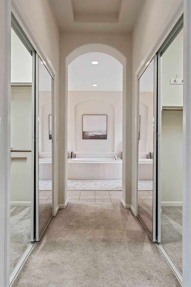 hallway featuring a tray ceiling, carpet flooring, arched walkways, and recessed lighting