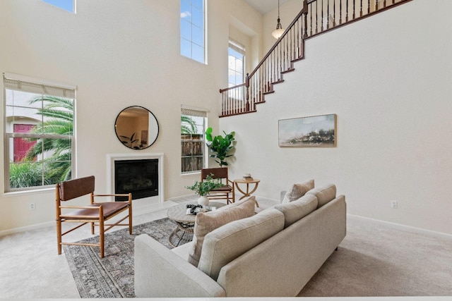 carpeted living area with a fireplace with raised hearth, a high ceiling, and baseboards