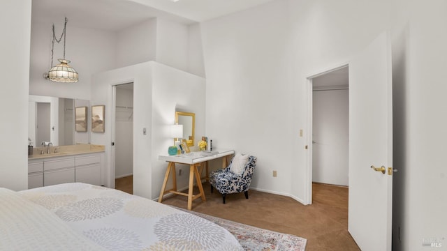 carpeted bedroom featuring baseboards, a towering ceiling, a sink, a walk in closet, and a closet