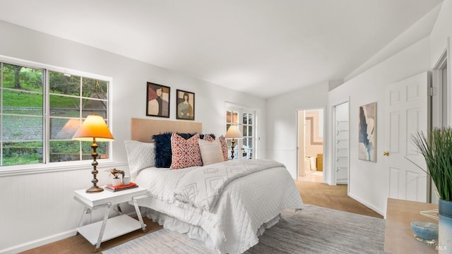 carpeted bedroom featuring ensuite bathroom, multiple windows, and baseboards