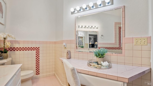 bathroom with a wainscoted wall, vanity, toilet, and tile walls