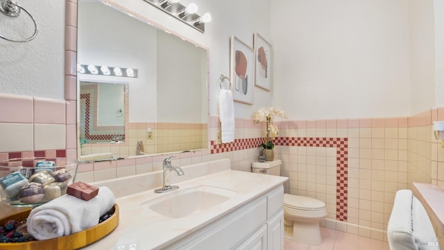 bathroom with wainscoting, toilet, tile patterned flooring, vanity, and tile walls