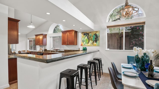 kitchen featuring light tile patterned floors, brown cabinets, a kitchen breakfast bar, pendant lighting, and a sink