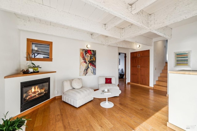 living area featuring a glass covered fireplace, beamed ceiling, stairs, and light wood-style floors