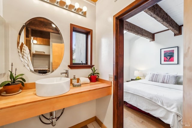 bathroom with connected bathroom, baseboards, beam ceiling, wood finished floors, and a sink