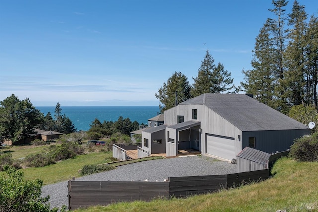 view of front facade featuring an attached garage, gravel driveway, an outdoor structure, and a water view