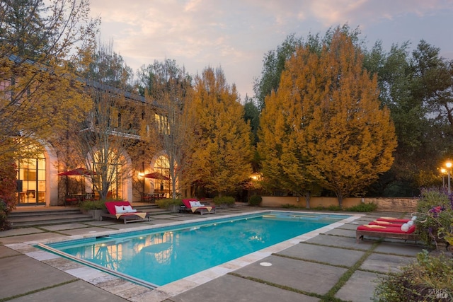 pool at dusk with a patio and a fenced in pool