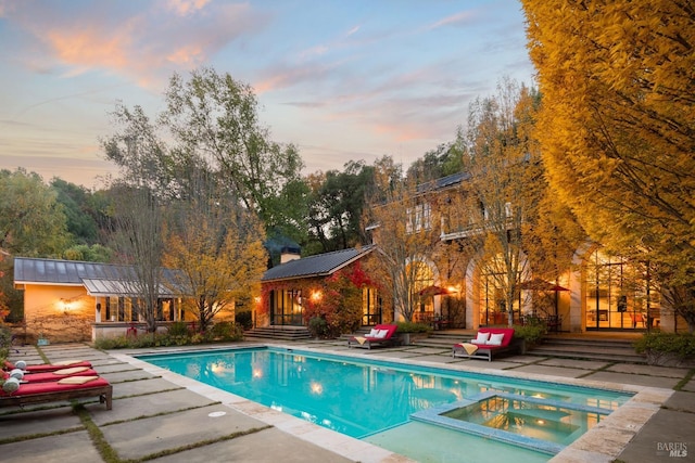 pool at dusk with a pool with connected hot tub and a patio area