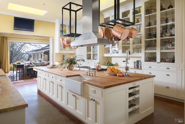 kitchen featuring island range hood, a sink, wood counters, white cabinets, and backsplash