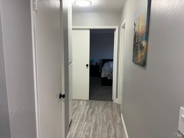 corridor with a textured ceiling and light hardwood / wood-style floors