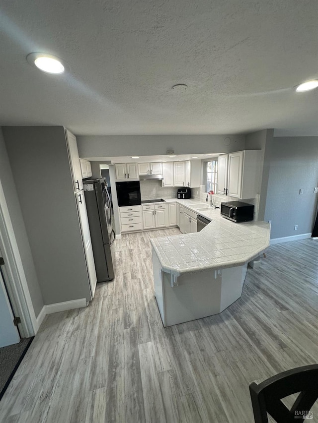 kitchen featuring appliances with stainless steel finishes, white cabinetry, tile counters, kitchen peninsula, and light wood-type flooring