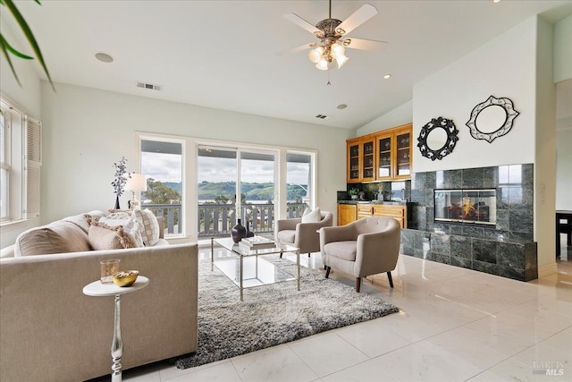 living room with ceiling fan, a mountain view, vaulted ceiling, and a tile fireplace