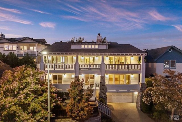 back house at dusk featuring a balcony and a garage