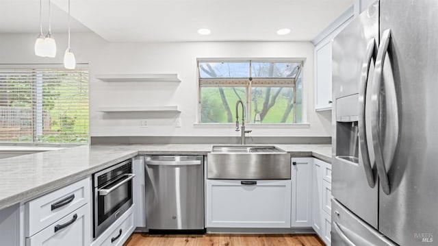 kitchen featuring appliances with stainless steel finishes, white cabinetry, sink, hanging light fixtures, and light stone countertops