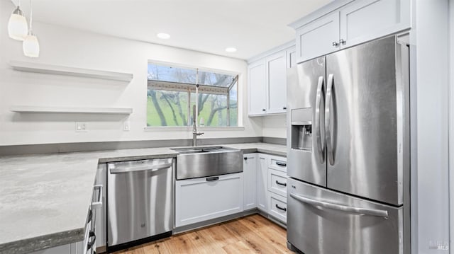 kitchen with sink, hanging light fixtures, stainless steel appliances, light hardwood / wood-style floors, and white cabinets