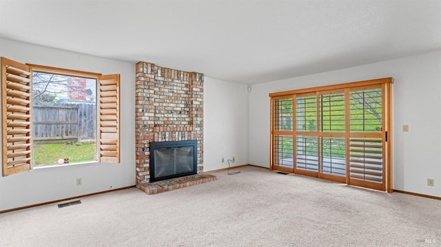 unfurnished living room featuring a brick fireplace, carpet floors, and a wealth of natural light