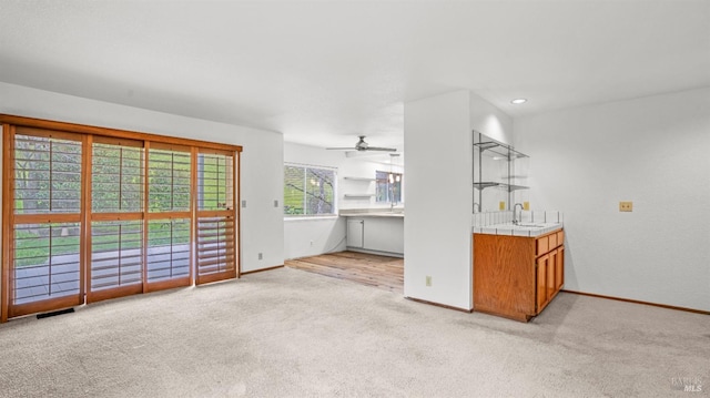 unfurnished living room with sink, light colored carpet, and ceiling fan