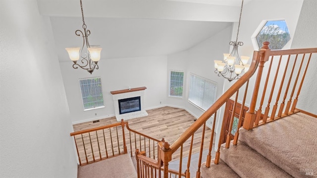 staircase featuring a fireplace, a chandelier, high vaulted ceiling, and hardwood / wood-style floors