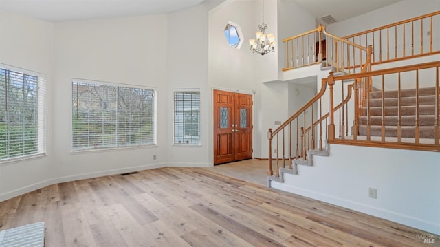 entrance foyer featuring a towering ceiling, light hardwood / wood-style flooring, and a notable chandelier