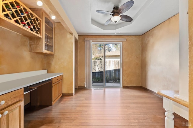 interior space featuring a raised ceiling, ceiling fan, built in desk, and light hardwood / wood-style floors