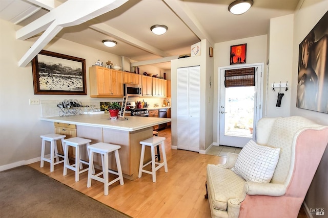 kitchen featuring appliances with stainless steel finishes, a kitchen breakfast bar, light hardwood / wood-style floors, kitchen peninsula, and beamed ceiling