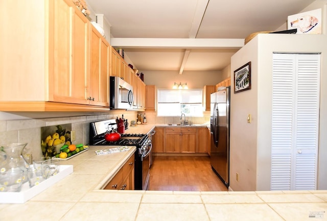 kitchen with sink, tile counters, beamed ceiling, stainless steel appliances, and backsplash