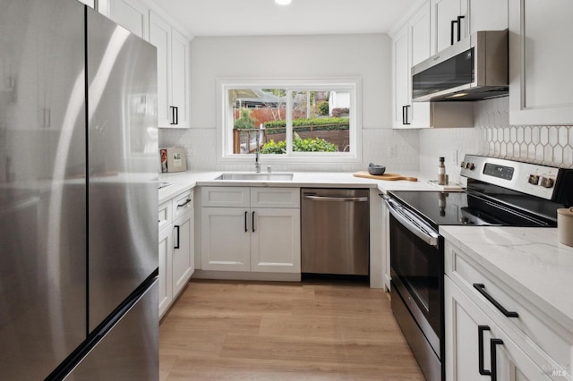 kitchen with backsplash, stainless steel appliances, light stone counters, light hardwood / wood-style floors, and white cabinets