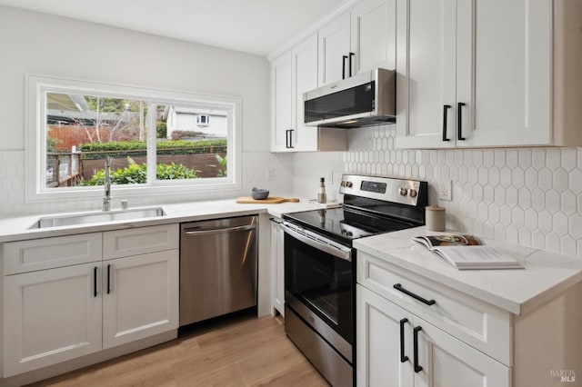 kitchen featuring sink, backsplash, stainless steel appliances, light stone countertops, and white cabinets