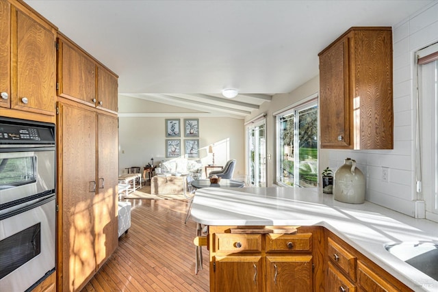 kitchen featuring lofted ceiling with beams, sink, double oven, and light hardwood / wood-style flooring