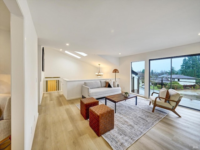 living room with vaulted ceiling with skylight, a chandelier, and light hardwood / wood-style floors