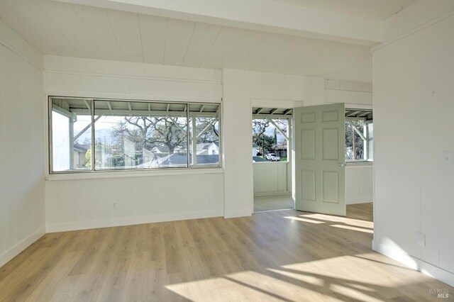 spare room with a healthy amount of sunlight, beam ceiling, and light hardwood / wood-style flooring