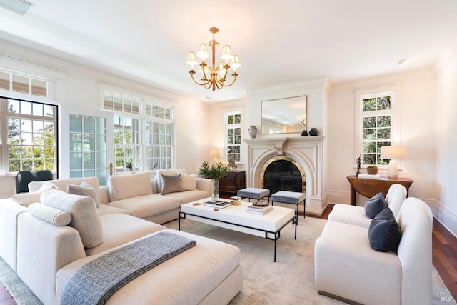 living area featuring baseboards, a glass covered fireplace, crown molding, a notable chandelier, and light wood-type flooring