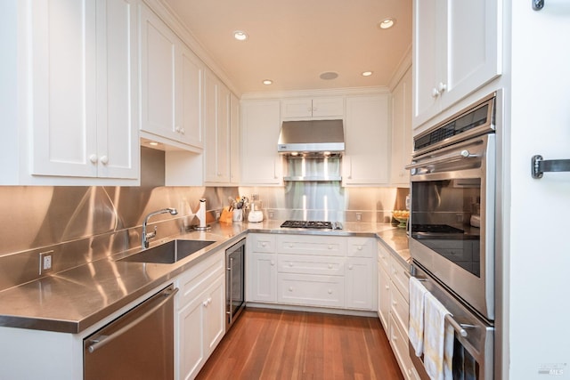 kitchen with stainless steel appliances, white cabinetry, sink, and exhaust hood