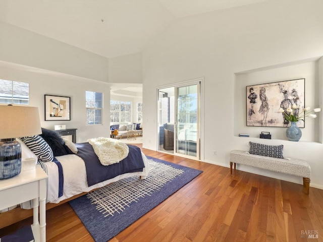 bedroom with hardwood / wood-style floors, a high ceiling, and access to exterior