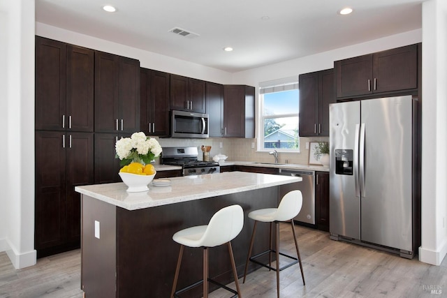 kitchen featuring stainless steel appliances, a center island, dark brown cabinetry, and a breakfast bar