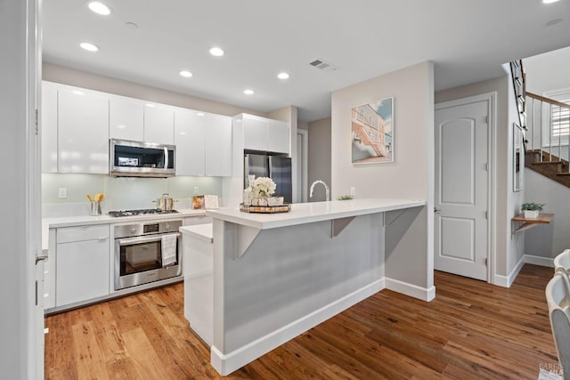 kitchen featuring white cabinetry, appliances with stainless steel finishes, a kitchen breakfast bar, kitchen peninsula, and light hardwood / wood-style floors