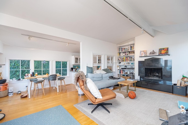 living room with a tile fireplace, lofted ceiling with beams, wood-type flooring, track lighting, and built in shelves