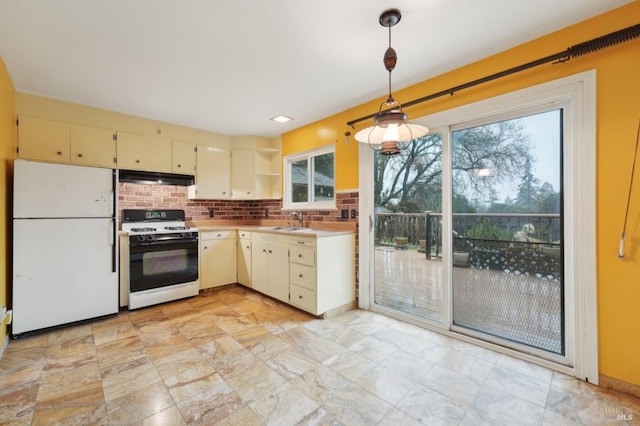 kitchen with sink, hanging light fixtures, decorative backsplash, range with gas cooktop, and white fridge