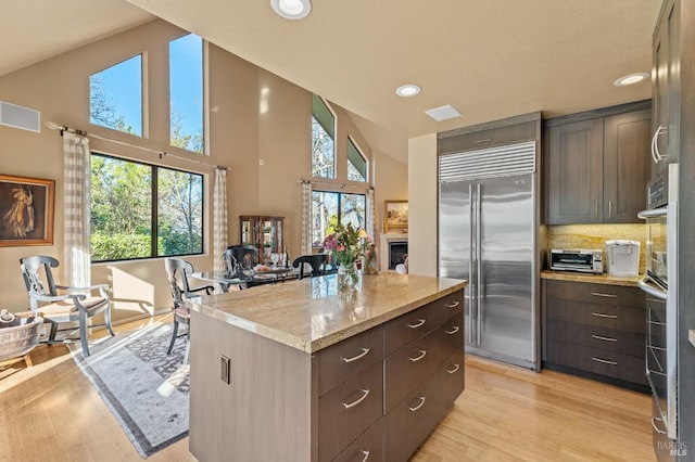 kitchen with built in refrigerator, a healthy amount of sunlight, a center island, and dark brown cabinetry