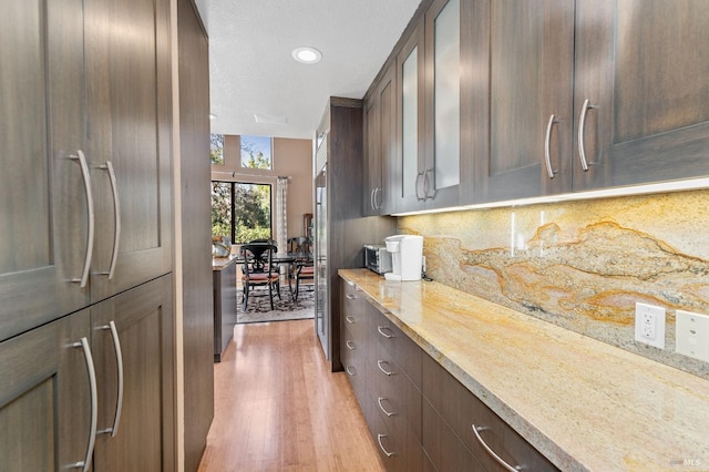 kitchen featuring dark brown cabinetry, light stone counters, tasteful backsplash, paneled fridge, and light hardwood / wood-style floors