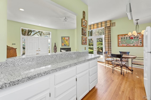 kitchen featuring light hardwood / wood-style flooring, ceiling fan, light stone counters, white cabinets, and french doors