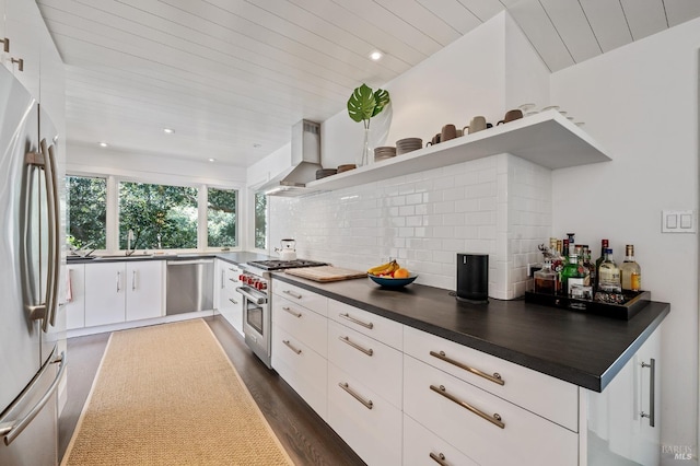 kitchen featuring white cabinetry, tasteful backsplash, appliances with stainless steel finishes, dark hardwood / wood-style floors, and wall chimney range hood